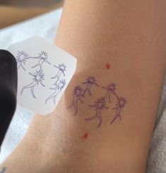 a person with tattoos on their legs and one hand holding a piece of paper that has dandelions drawn on it