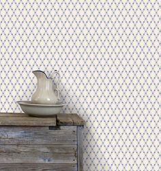 a white vase sitting on top of a wooden table next to a wallpapered wall