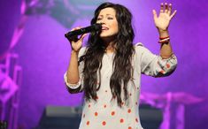 a woman singing into a microphone while holding her hands up in the air with one hand