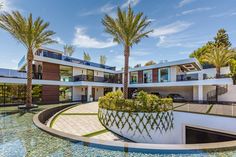 the house is surrounded by palm trees and water features a circular fountain that sits in front of it