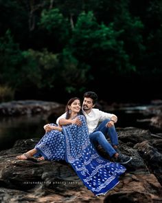 a man and woman sitting on rocks near water