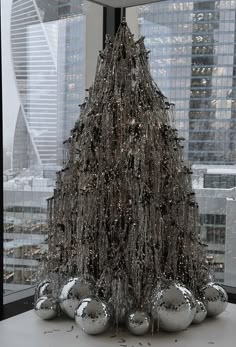 a christmas tree made out of silver balls in front of a window with skyscrapers behind it