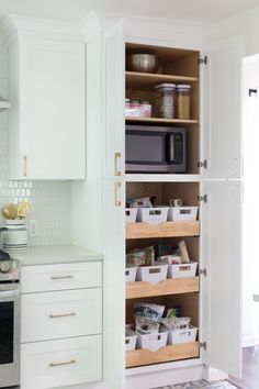 an open pantry door in a kitchen with white cabinets and drawers filled with food items