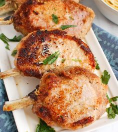 three pork chops on a white plate with parsley sprinkled around them