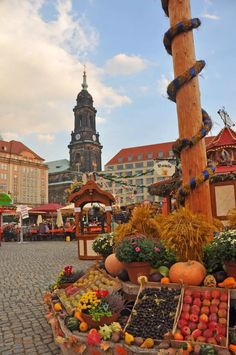 an outdoor fruit and vegetable stand on a cobblestone street in front of a clock tower