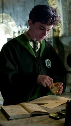 a young man in a harry potter costume is holding a glass and looking at it