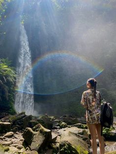 a woman standing in front of a waterfall with a rainbow