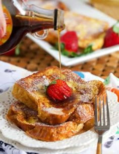 someone pouring syrup on french toast with strawberries and other food items in the background