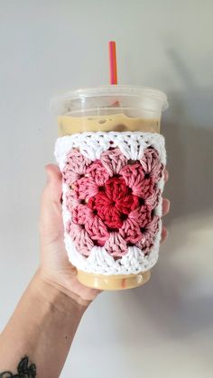 a person holding up a cup with a crochet pattern on the side and a straw in it