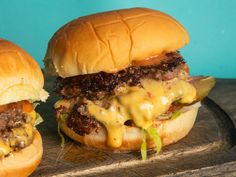 two hamburgers with cheese and pickles on a cutting board next to each other