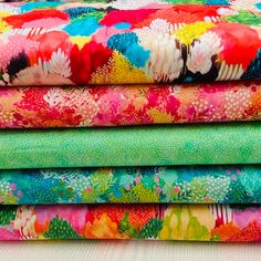 a stack of colorful fabrics sitting on top of a wooden table next to each other