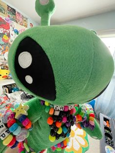 a green stuffed animal with lots of buttons on it's chest and eyes, standing in front of a bed