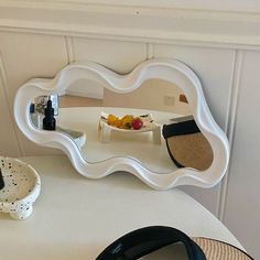 a white table topped with a mirror next to a bowl of fruit on top of a plate