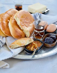 an assortment of breads and condiments on a silver plate with white cloth