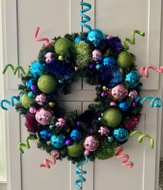 a christmas wreath with ornaments hanging from it's side and streamers on the front door