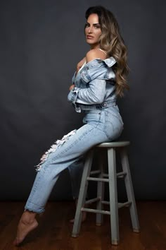 a woman sitting on top of a wooden stool wearing ripped jeans and high heeled shoes