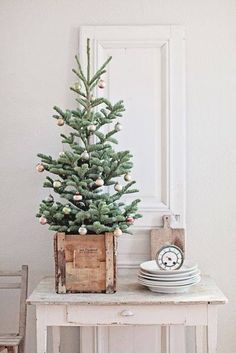 a small christmas tree sitting on top of a wooden table next to a white chair