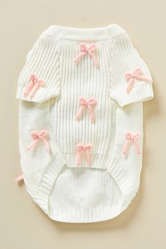 a white sweater with pink bows on the collar and sleeves, sitting on top of a table