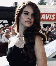 a woman with long dark hair standing in front of a crowd wearing a black dress