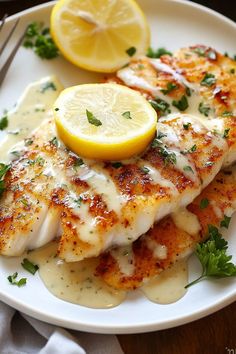 a white plate topped with fish covered in sauce and lemon wedges next to a fork