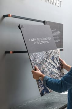 a person holding up a map in front of a sign that says a new destination for london