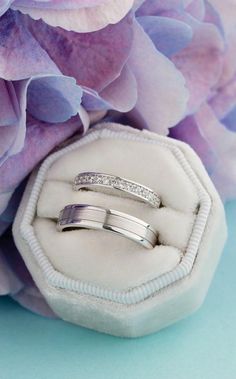 two wedding rings sitting on top of a white ring box next to purple and blue flowers