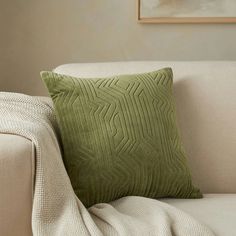 a green pillow sitting on top of a couch next to a white blanket and a painting