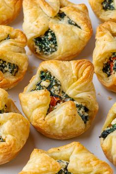 many small pastries with spinach and cheese on them sitting on a white surface