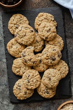 chocolate chip cookies on a slate board with bowls of oatmeal in the background