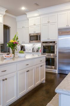 a large kitchen with white cabinets and stainless steel appliances, along with a bowl of fruit on the counter