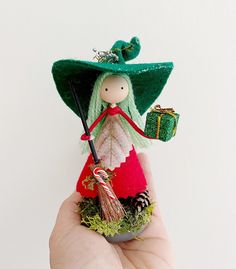 a hand holding a small doll with a green hat and red dress on it's head