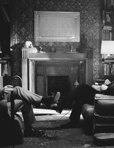 black and white photograph of two men sitting in front of a fire place with bookshelves