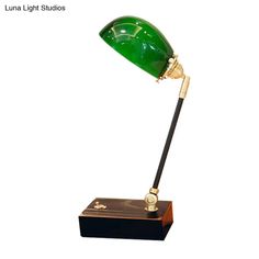 a green glass desk lamp sitting on top of a wooden stand with a black base