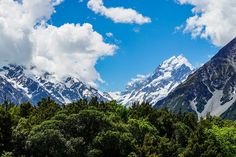 the mountains are covered in snow and green trees under a blue sky with white clouds