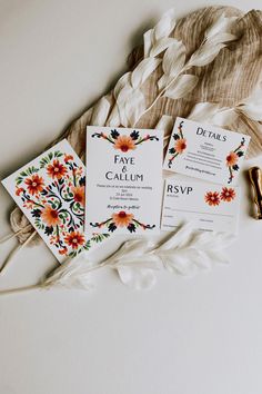 the wedding stationery is laid out on top of some white fabric and flowers, including an orange flower