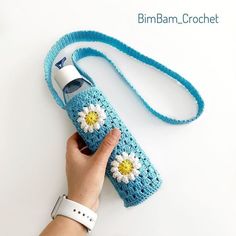 a hand holding a blue crocheted water bottle with a white flower on it