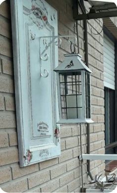 a white bird feeder hanging from the side of a brick building next to a window