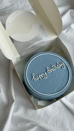 a blue birthday cake in a box on a white sheeted surface with the words happy birthday written on it