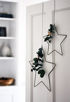 two metal stars hanging from the side of a white door with green leaves on them