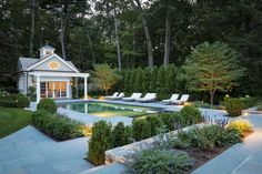 an outdoor pool surrounded by trees and bushes with lounge chairs around it, in front of a gazebo