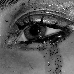 a woman's eye with black and white glitters on her lashes, looking down at the ground