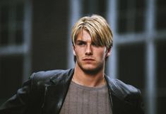 a young man with blonde hair wearing a black leather jacket and looking at the camera