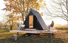 a woman sitting on top of a wooden platform next to a black tent in the woods