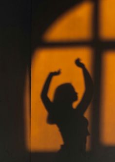 the shadow of a woman standing in front of a window with her arms raised up