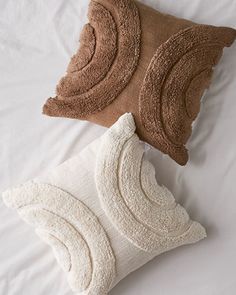 two pillows on top of a bed with white sheets and brown throw pillows next to each other