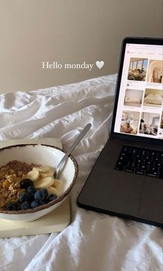 an open laptop computer sitting on top of a bed next to a bowl of cereal