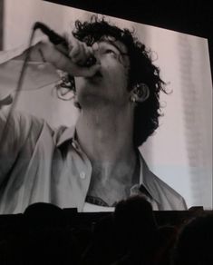 a man holding a microphone up to his mouth while standing in front of a large screen