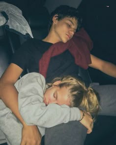 two young children sleeping on the back of a car seat with their arms wrapped around each other