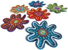 four crocheted flowers on a white surface with one flower in the center and two are brightly colored