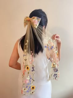 a woman wearing a veil with flowers on it and a bow in her hair is seen from behind